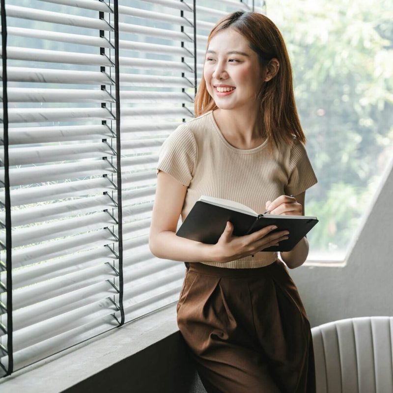 smiling-asian-woman-holding-a-note-in-hand-and-standing-near-window-startup-business-asian-woman-onl.jpg